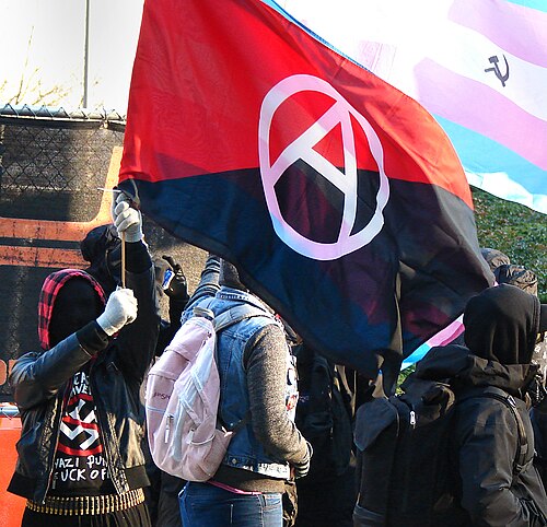 Antifa activists iwth a modified anarchist red and black flag and a transgender pride flag in 2017 pic wikipedia